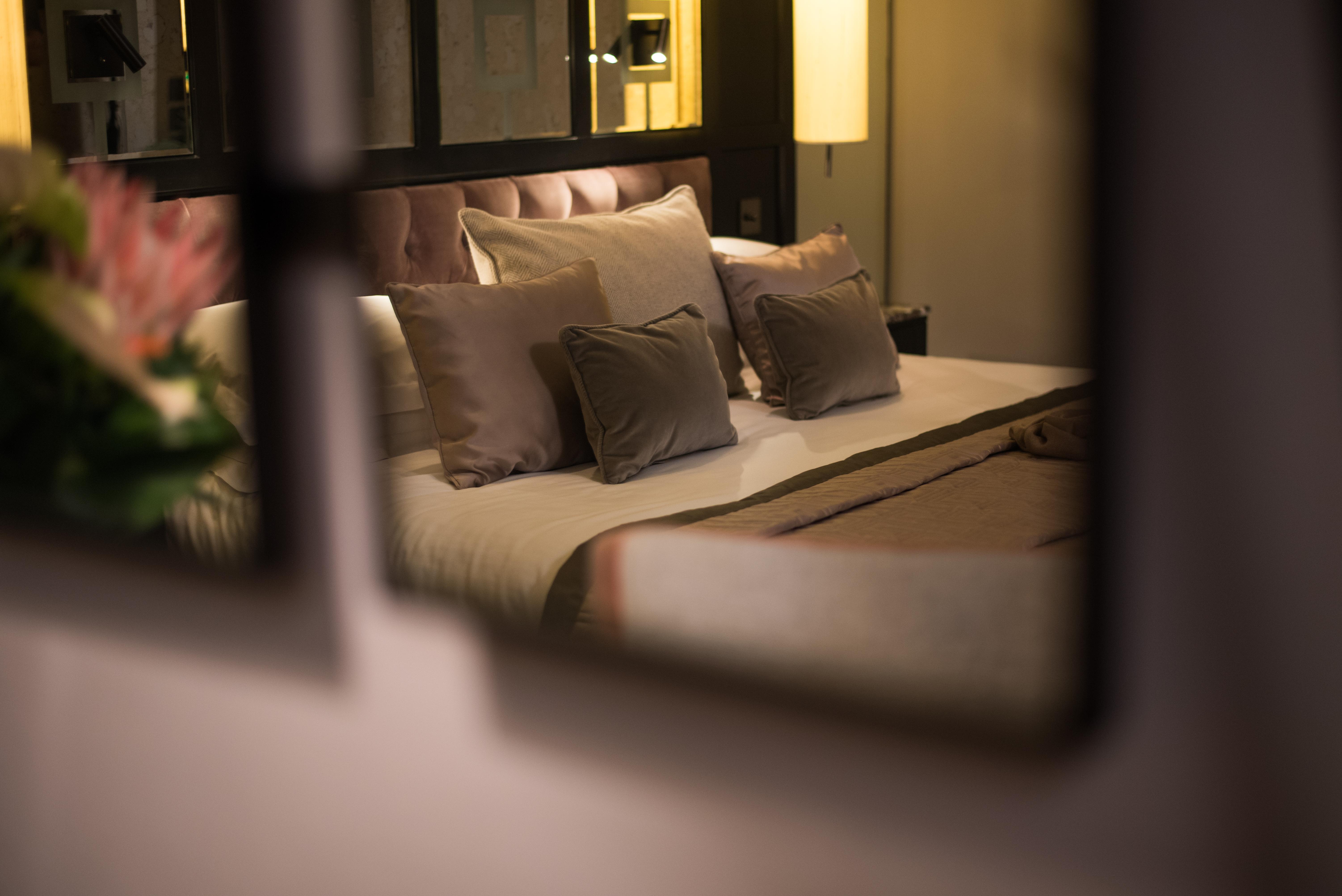 The Fitzwilliam Hotel Belfast Exterior foto The photo shows a cozy and elegantly decorated bedroom. The focal point is a plush bed with soft, neutral-colored bedding and several decorative pillows arranged neatly on it. The room has a warm ambiance, enhanced by a standing lamp that provides so