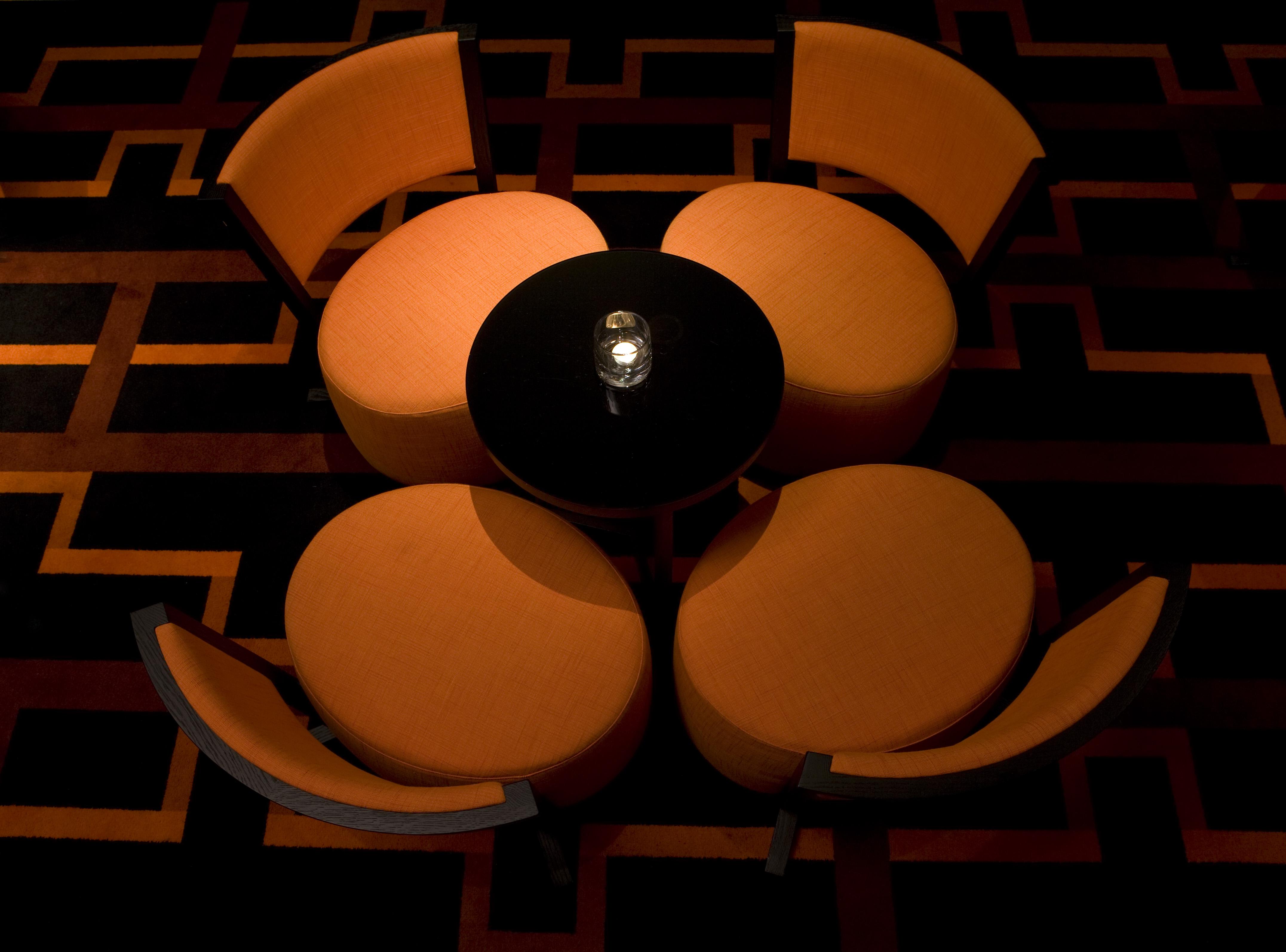 The Fitzwilliam Hotel Belfast Exterior foto The image shows a small seating arrangement consisting of four orange chairs arranged around a circular black table. The setting appears to be in a dimly lit area, emphasizing the warm tones of the chairs and the dark finish of the table. The floor d